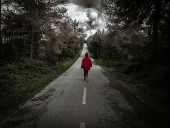 Rear view of woman wearing red hooded jacket while walking on road in forest
