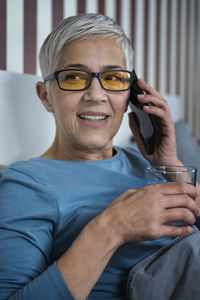 Blue-light blocking glasses. mature woman talking over the phone relaxing at home before sleep