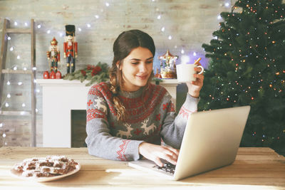 Smiling woman with cup of coffee using laptop at christmas time