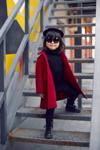 Korean girl in a red coat and beret stands on the iron staircase the street in autumn.