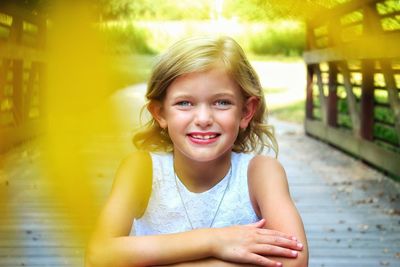 Portrait of smiling girl sitting on footbridge at park