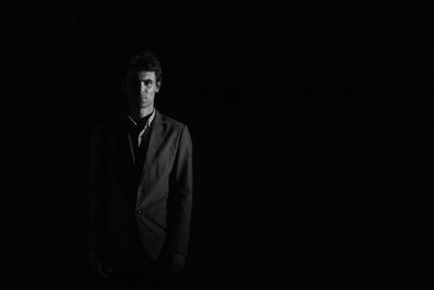 Portrait of businessman standing in dark against black background