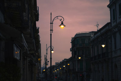 Low angle view of illuminated street light against buildings at sunset