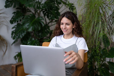 Woman freelancer working on laptop surrounded by exotic houseplants in home garden. cozy workplace.