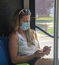 Young woman using mobile phone while sitting on window