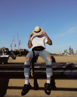 Full length of man sitting on railing against blue sky