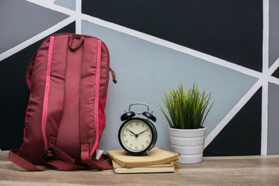 Backpack by alarm clock over books on table against wall