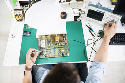High angle view of technician checking circuit board at table in electronics industry