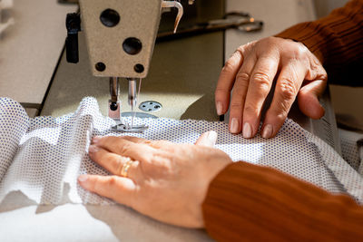 Cropped unrecognizable senior seamstress sitting at sewing machine and stitching piece of cloth while working in workshop