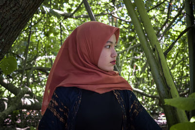 Portrait of young woman looking away against trees