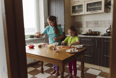 Siblings making pizza together in kitchen at home