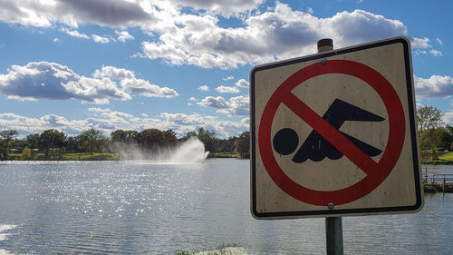 Road sign by lake against sky