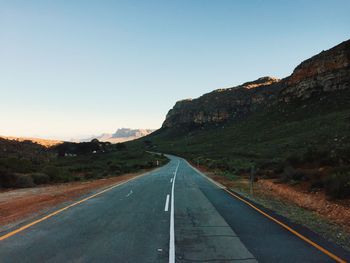 Road leading towards mountains against clear sky