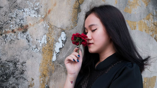 Portrait of beautiful woman holding flower against wall