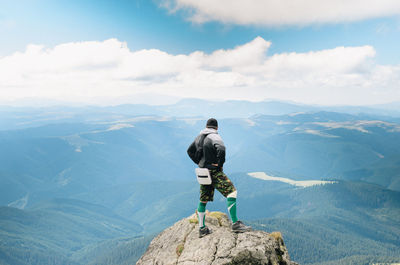 Rear view of man standing on mountain against cloudy sky