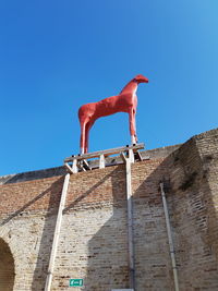 Low angle view of lizard on wall against clear blue sky