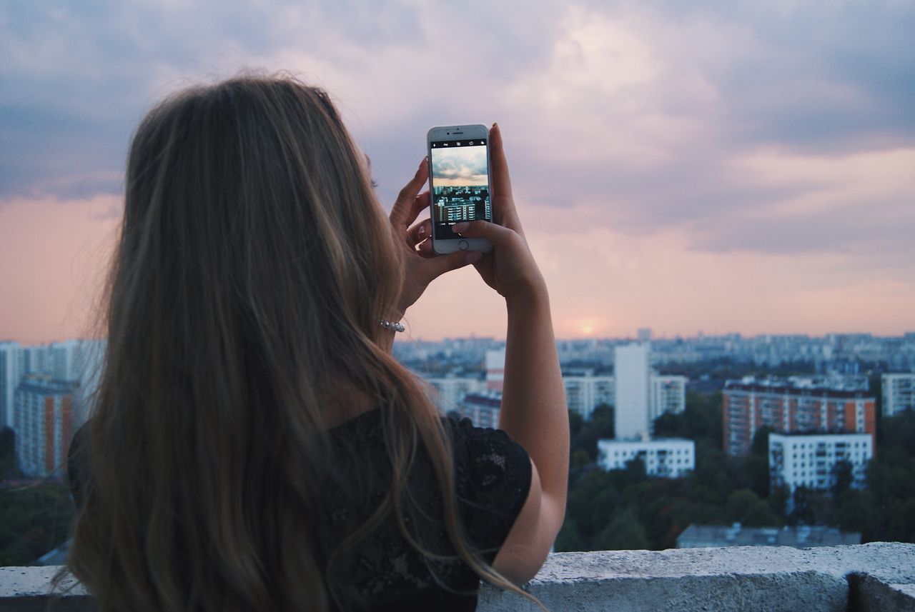 REAR VIEW OF WOMAN PHOTOGRAPHING THROUGH CITYSCAPE