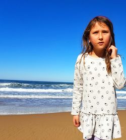 Girl looking away while standing at beach against blue sky