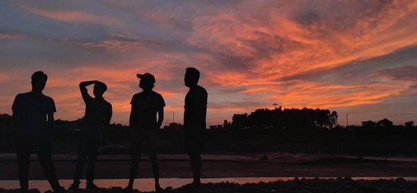 Silhouette people standing against orange sky