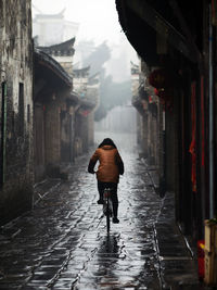 Rear view of man walking on wet road during rainy season