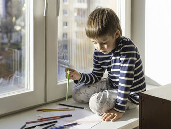 Boy holding pencil sitting by window
