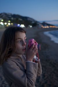 Portrait of young girl holding camera at beach