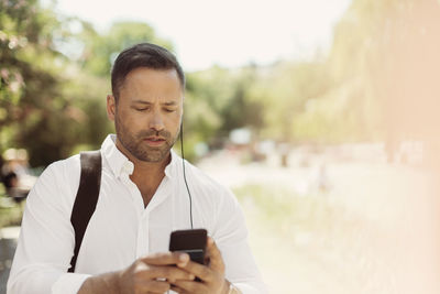 Businessman using smart phone in park during summer