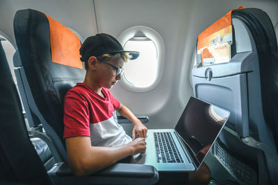 Side view of boy using laptop while sitting in airplane
