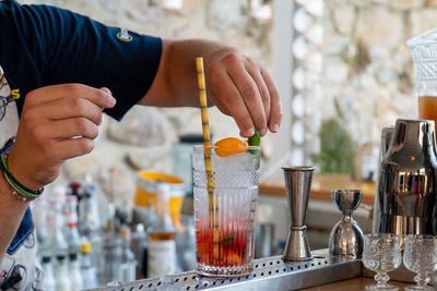 Male bartender adding a garnish to a colorful red and pink cocktail with a paper straw.