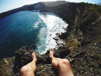 Low section of person against sea on cliff during sunny day