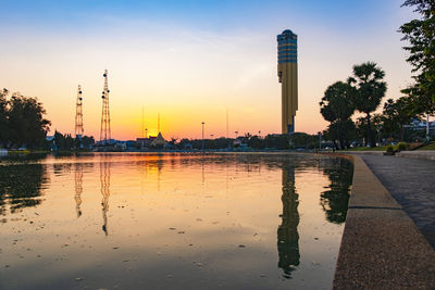 Scenic view of lake by buildings against sky at sunset