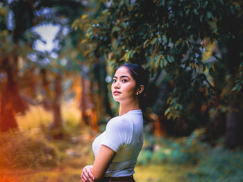 Portrait of young woman standing by plant outdoors