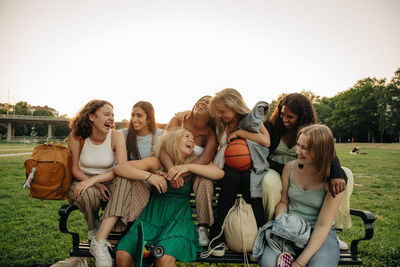 Cheerful multiracial teenage girls enjoying while sitting on bench at park