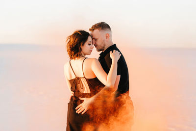 Happy couple on beach against sky during sunset