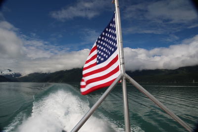 American flag on boat against cloudy sky