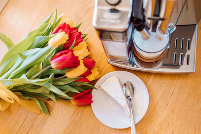 Cup of coffee with milk, piece of cake and tulips flowers on wooden kitchen table. freshly brewed 