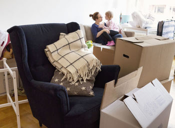 Boxes and armchair in apartment, mother with daughter in background