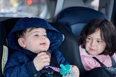 Siblings in car seats having snacks in the back seat of a car on a rainy day