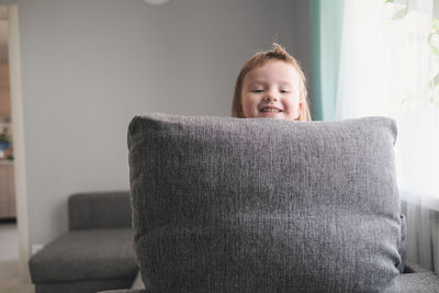 Kid toddler builds house from pillows on sofa in living room, lifestyle and games in real interior