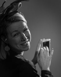 Close-up portrait of smiling woman using phone against gray background