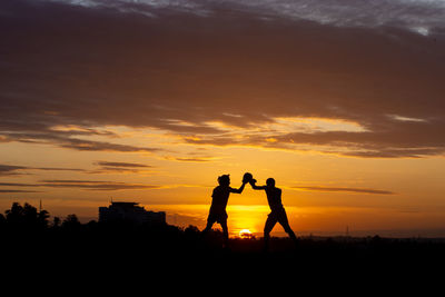 Silhouette of two man boxing against sky during sunset