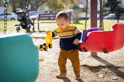 Funny baby boy playing at outdoors playground. toddler plays with toy car. sunny day