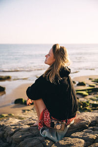 Full length of woman sitting on rock at beach