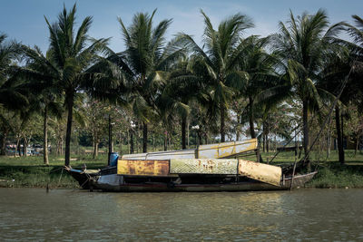 Boats moored on river by trees against sky