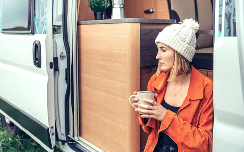 Woman drinking coffee sitting at the door of a campervan