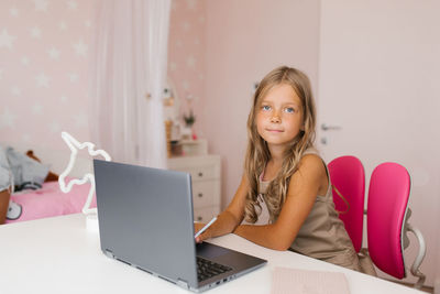 Little girl uses a video tutorial on a laptop, sitting at a table in a room