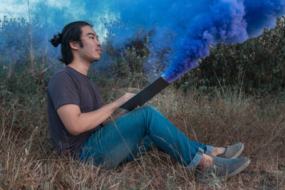 Side view of young man using mobile phone while sitting on land