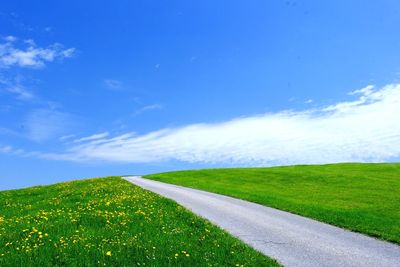 Country road on grassy field against cloudy sky