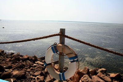 Inflatable ring on rope fence pole over groyne in sea against sky