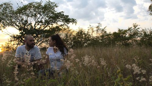 Friends standing on field by trees against sky